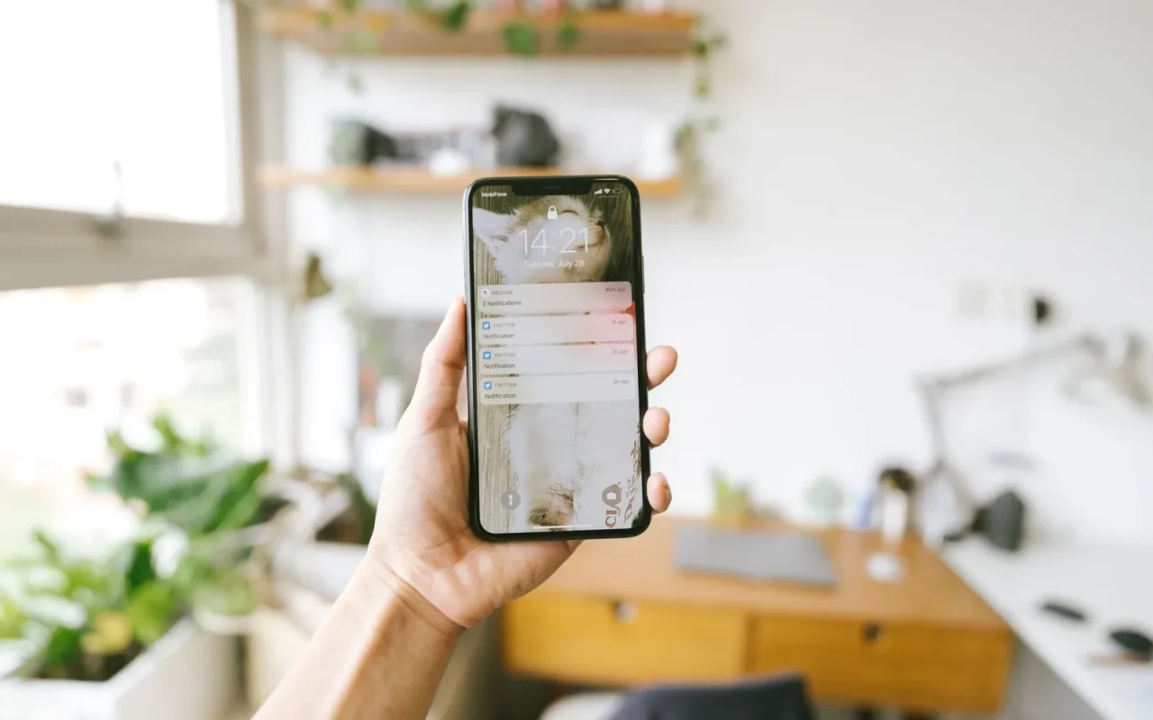 Homeowner checking a robot mower app notification on a phone beside a green lawn
