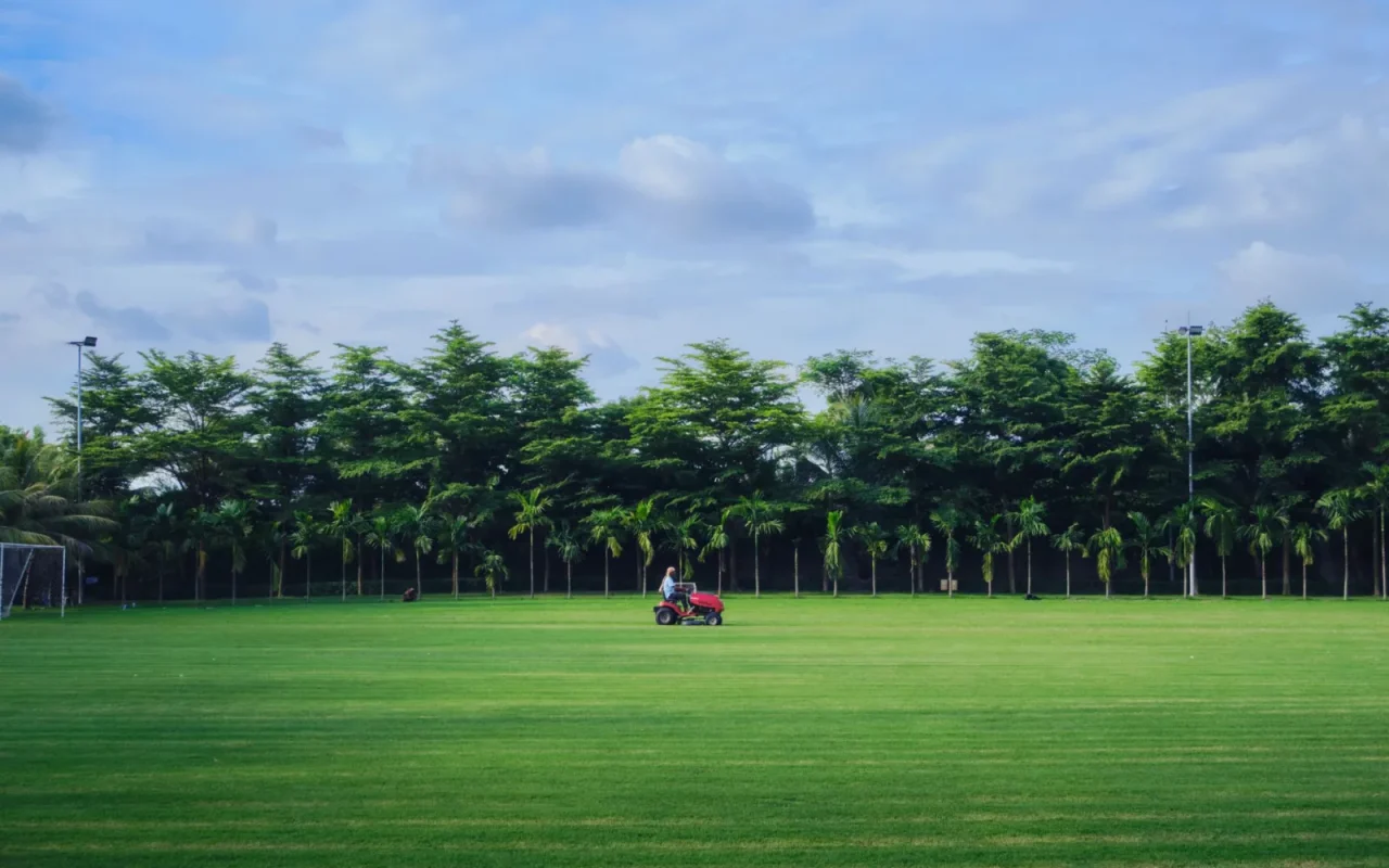 Robot mower crossing a lawn boundary near a flower bed on a wide green yard