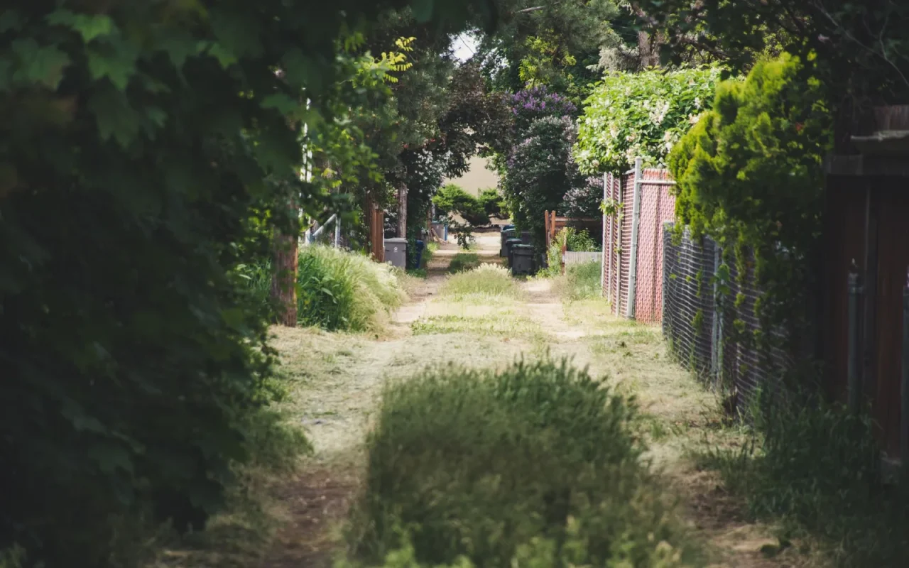 Robot mower driving through a narrow grass passage between a fence and garden bed