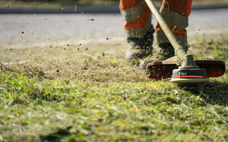 A lawn care worker pushing a mower across a green suburban front yard