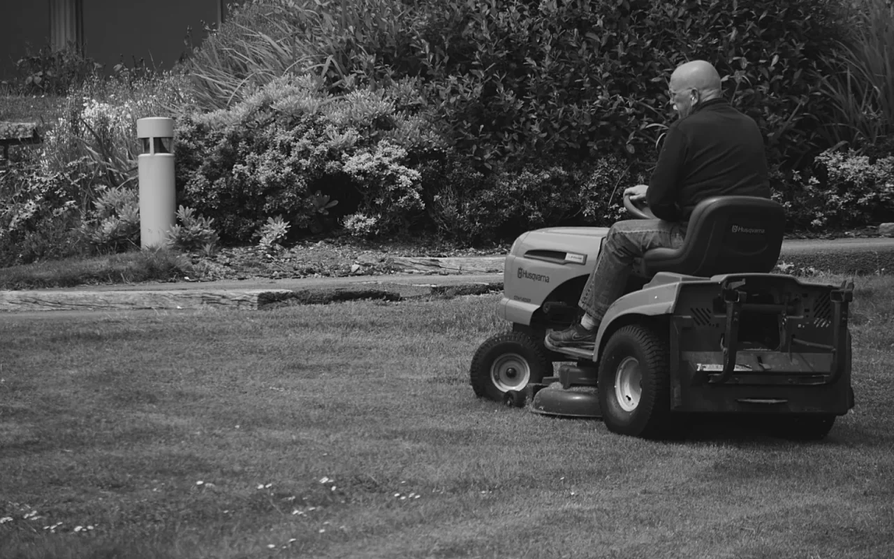 A green riding lawn mower parked on a freshly cut suburban lawn in sunlight