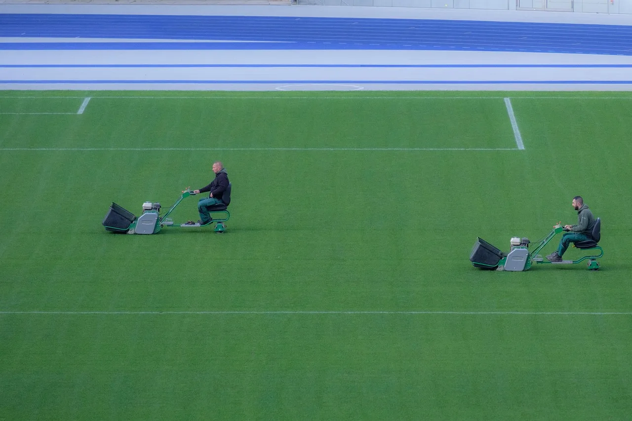 A budget robot lawn mower parked on a small tidy green lawn near a fence