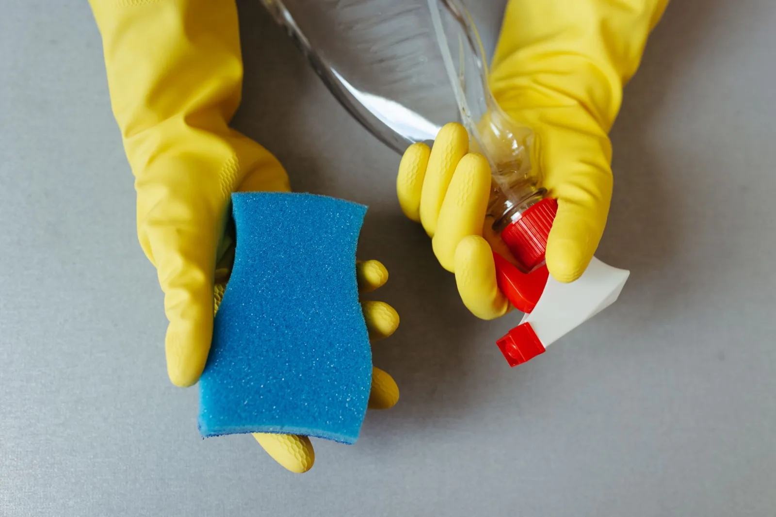 Gloved hand scraping packed clippings from the underside of a robot lawn mower