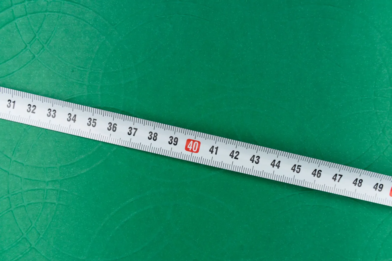 Hands measuring the length of a green backyard lawn with a tape measure