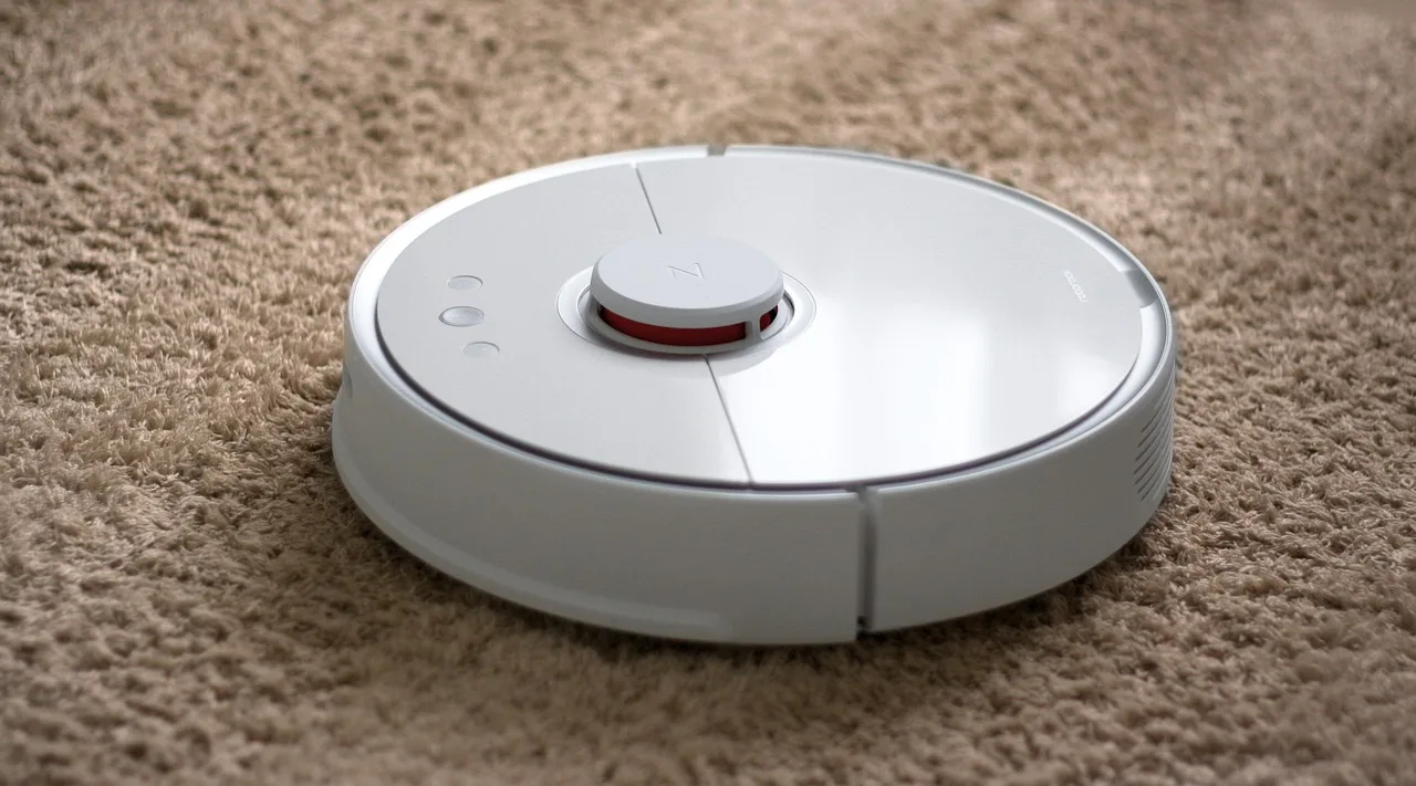 A round robot vacuum cleaning a hardwood living room floor at home